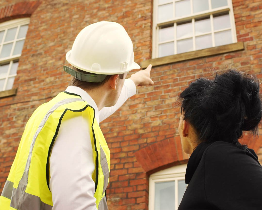 man in a hard hat with a woman looking at a brick building